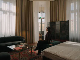 woman sitting on hotel room bed with large windows and stylish interior design. Chateau Royal Berlin 